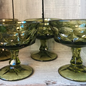 May include: Four green glass dessert bowls with a diamond pattern. The bowls are on a wooden surface.