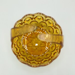 May include: An overhead view of a vintage amber-colored glass basket. The basket has a scalloped edge and a starburst pattern in the center. It features a handle made of the same amber glass material.