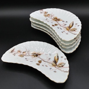May include: Set of five white porcelain half-moon shaped serving plates with a gold rim. Each plate features a brown and gold floral design.