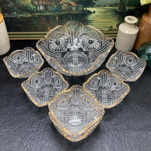 May include: A set of six clear glass bowls with gold trim. The bowls are all different sizes and shapes, and they are arranged in a circle on a black surface.
