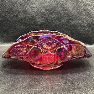 May include: A red iridescent glass bowl with a scalloped edge and a geometric pattern. The bowl is made of carnival glass and has a vintage look.