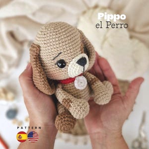 Puede incluir: Un juguete de perro tejido a ganchillo en beige y marrón, con un collar rojo y una etiqueta blanca. El perro tiene ojos negros y una nariz negra. El texto "Pippo el Perro" es visible. La palabra "PATTERN" también es visible, junto con las banderas de España y Estados Unidos.