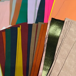 May include: A collection of rectangular sheets of faux leather in a wide variety of colors and textures. The assortment includes solid matte shades like pink, orange, green, and navy, alongside metallic finishes, speckled patterns, and textured surfaces.