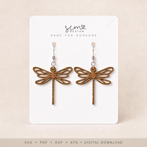 May include: A pair of brown wooden dragonfly earrings with silver-toned metal hooks displayed on a white card featuring the text scm DESIGN MADE FOR SOMEONE. The bottom of the card includes the text SVG PDF DXF EPS DIGITAL DOWNLOAD.