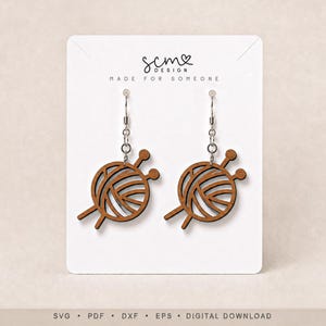 May include: A pair of brown wooden earrings shaped like a ball of yarn with two knitting needles. The earrings are attached to a white display card featuring the text SCM DESIGN MADE FOR SOMEONE at the top and SVG PDF DXF EPS DIGITAL DOWNLOAD.