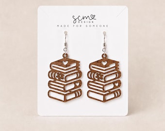 Könnte beinhalten: Ein Paar braune Holz-Ohrhänger in Form eines Stapels aus vier Büchern. Jeder Ohrring weist ausgeschnittene Details auf, darunter ein kleines Herz und eine Blume auf den Buchrücken. Die Ohrringe hängen an silberfarbenen Metallhaken auf einer weißen Karte.