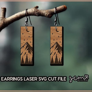 May include: A pair of wooden earrings with a laser-cut design of a mountain range, crescent moon, and stars. The earrings are hanging from a branch.
