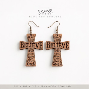 May include: A pair of brown wooden cross-shaped earrings featuring engraved text including the word BELIEVE, grace, faith, hope, trust, Jesus, Christ, blessed, light, glory, and AMEN. The earrings are suspended from bronze-colored metal hooks.
