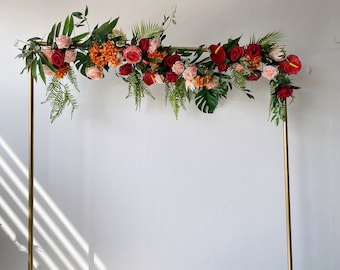 Könnte beinhalten: Ein goldener Metallbogen, der mit einer Girlande aus roten, rosa und orangefarbenen Blumen, grünen Blättern und tropischem Laub geschmückt ist.