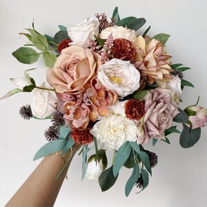 May include: A bouquet of artificial flowers in shades of pink, peach, and cream. The bouquet includes roses, hydrangeas, and other floral elements.