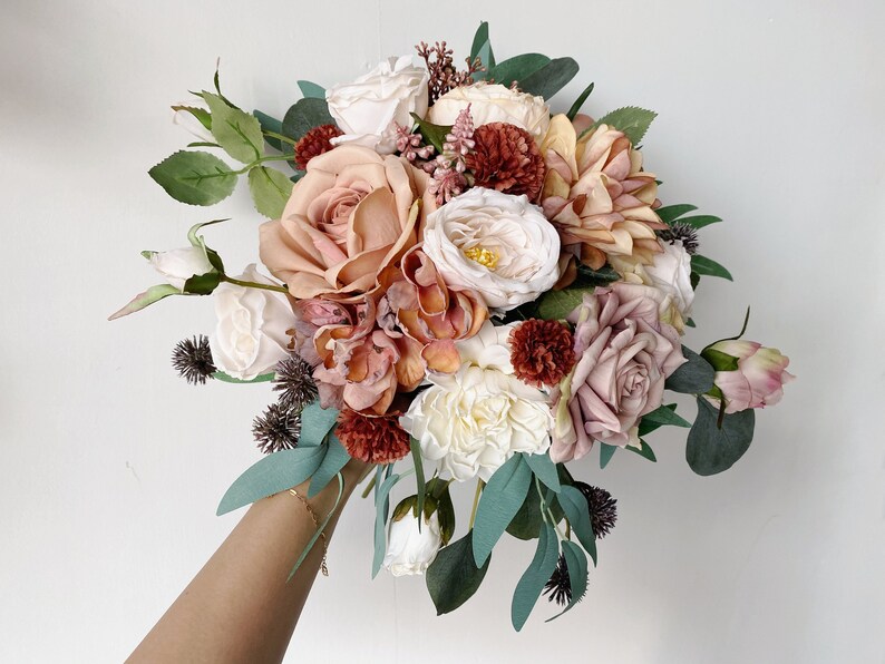 May include: A bouquet of artificial flowers in shades of pink, peach, and cream. The bouquet includes roses, hydrangeas, and other floral elements.