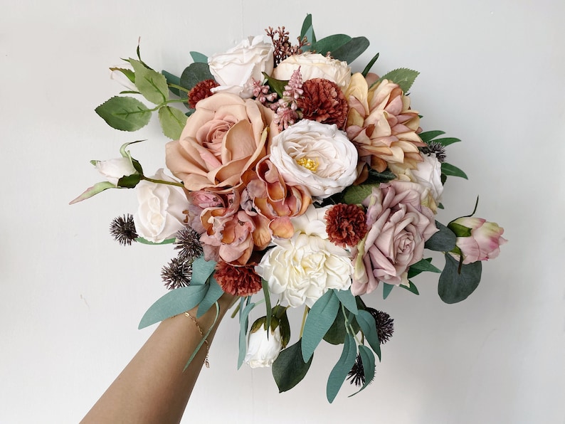 May include: A bouquet of artificial flowers in shades of pink, peach, and cream. The bouquet includes roses, hydrangeas, and other floral elements. The flowers are arranged in a loose, natural style.