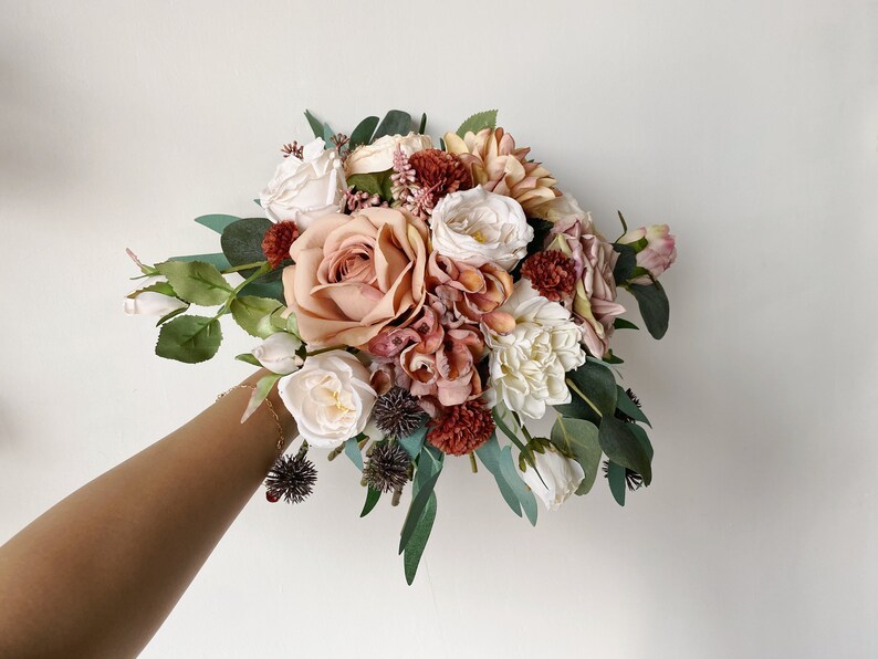 May include: A bouquet of artificial flowers in shades of blush, cream, and burgundy. The bouquet includes roses, dahlias, and eucalyptus.