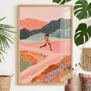 May include: A framed art print depicts a person running through a colorful landscape. The artwork features a runner in orange shorts and a pink top, set against a backdrop of layered mountains in shades of pink, green, and blue. The frame is made of light-colored wood.