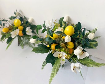 May include: Two bouquets of artificial flowers featuring white orchids, white tulips, and yellow lemons. The bouquets are arranged with green leaves and ferns.