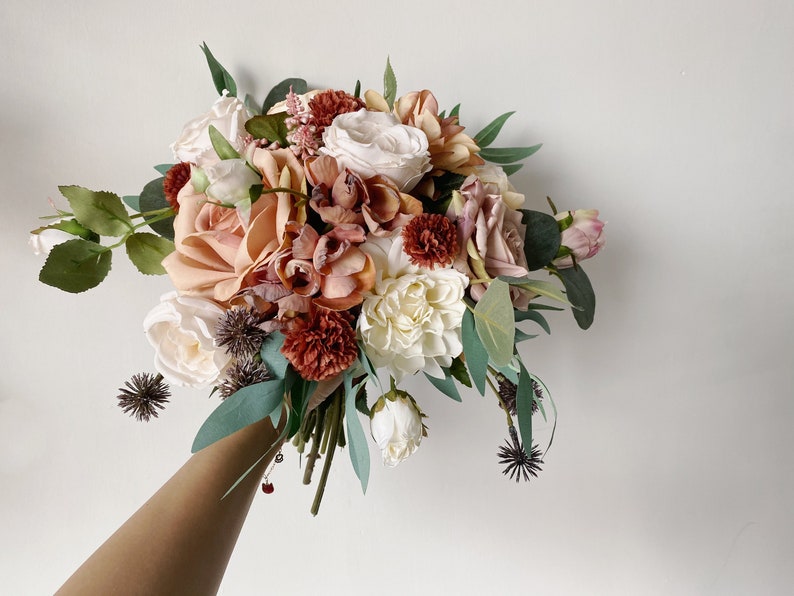 May include: A bouquet of artificial flowers in shades of peach, white, and burgundy. The bouquet includes roses, peonies, and other floral elements.