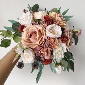 May include: A bouquet of blush pink, white, and rust colored artificial flowers with greenery. The bouquet includes roses, hydrangeas, and other floral accents.