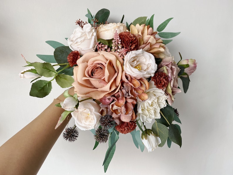 May include: A bouquet of blush pink, white, and rust colored artificial flowers with greenery. The bouquet includes roses, hydrangeas, and other floral accents.