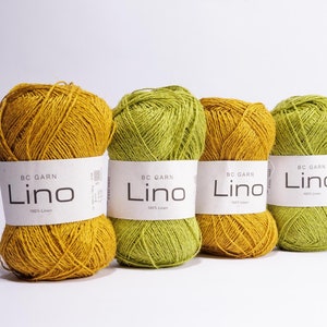 Könnte beinhalten: Vier Knäuel Garn in zwei Farben: Senfgelb und Olivgrün. Jedes Knäuel hat ein weißes Etikett mit der Aufschrift "BC Garn Lino 100% Leinen".