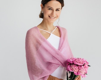 Könnte beinhalten: Eine Frau trägt einen transparenten, hellrosa Strickschal über einem weißen Kleid und hält einen Strauß rosa Pfingstrosen. Der Schal hat ein drapiertes Design. Die Frau lächelt, mit einem silbernen Stirnband und Ohrringen.