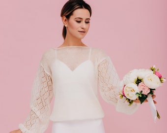 Può includere: Una donna indossa un maglione bianco lavorato a maglia con un motivo di pizzo sulle maniche e una gonna bianca. Tiene un mazzo di peonie bianche e rosa.