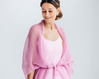 Könnte beinhalten: Eine Frau trägt einen hellrosa Strickcardigan über einem passenden rosa Schlupfkleid. Der Cardigan hat einen Gürtel in der Taille und ist aus einem zarten, luftigen Stoff gefertigt.