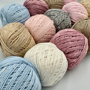 May include: A collection of yarn balls in various colors, including pink, beige, blue, and white. The yarn is made of natural fibers and has a textured appearance.