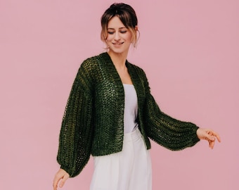 Peut inclure: Une femme portant un cardigan en tricot vert avec un pantalon blanc large et des sandales blanches.