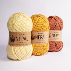 May include: Three skeins of DROPS Nepal yarn in yellow, orange, and brown. The yarn is made of wool and alpaca and is labeled "UNI COLOUR".