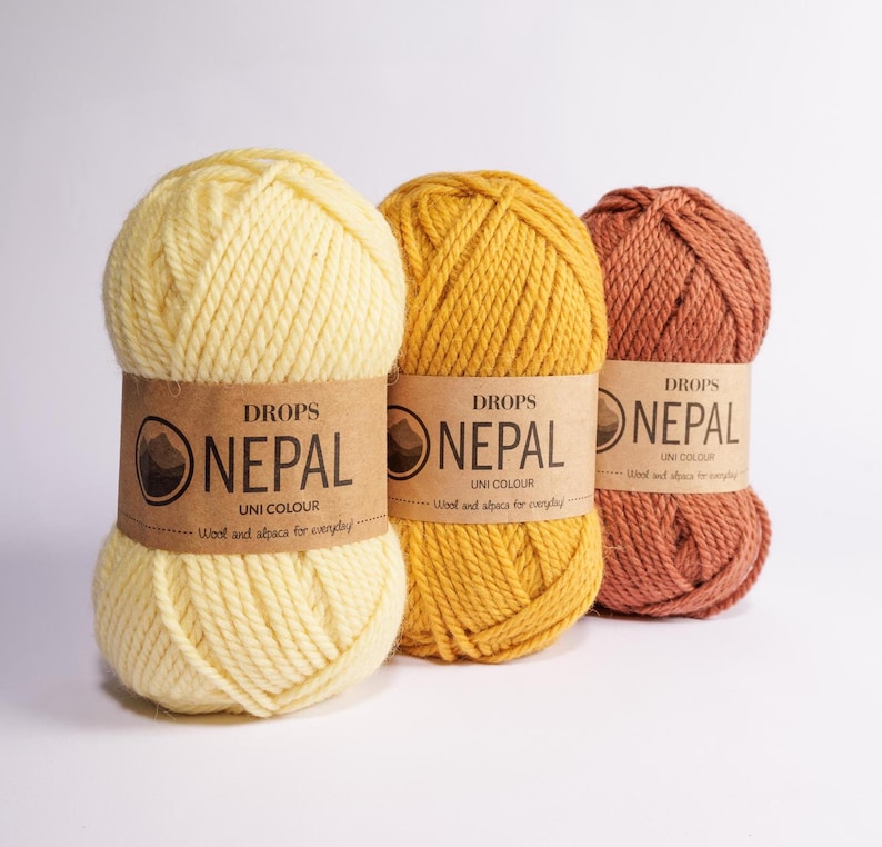 May include: Three skeins of DROPS Nepal yarn in yellow, orange, and brown. The yarn is made of wool and alpaca and is labeled "UNI COLOUR".