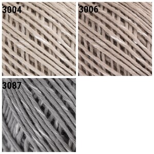 May include: Close-up of three skeins of yarn in beige and gray colors. The yarn is made of cotton and has a textured surface. The skeins are labeled with the numbers 3004, 3006, and 3087.
