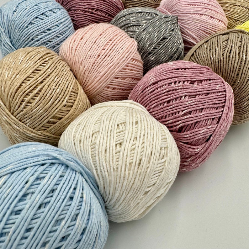 May include: A collection of balls of yarn in various colors, including light blue, beige, cream, pink, and gray. The yarn is made of a soft, textured material and is perfect for knitting or crocheting.