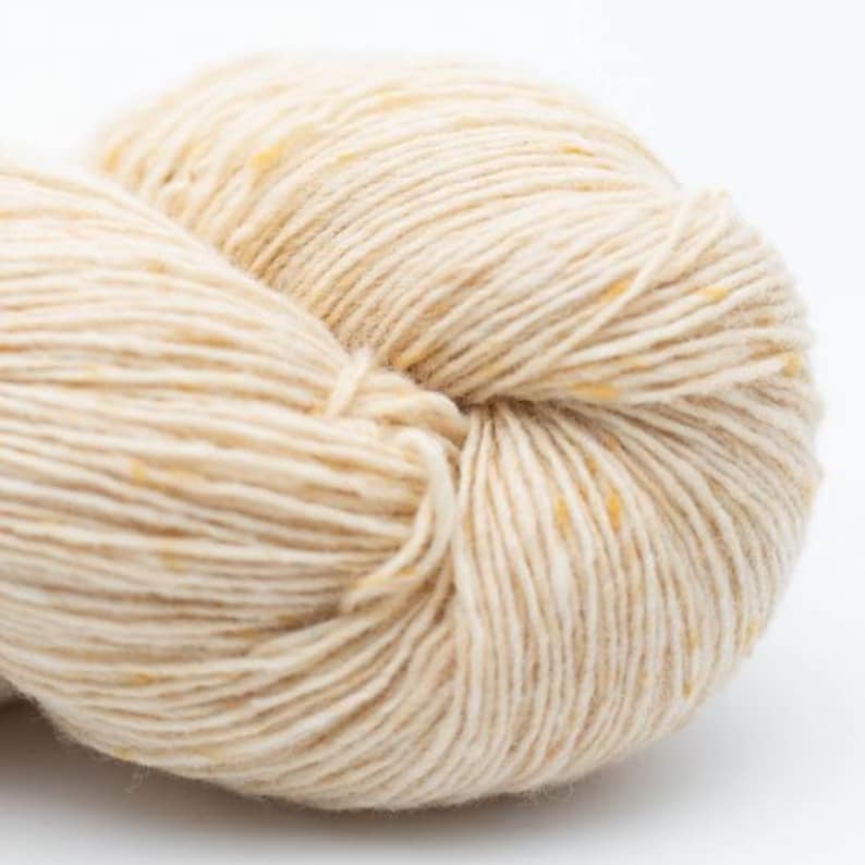 May include: A skein of cream-colored yarn with subtle flecks of yellow.