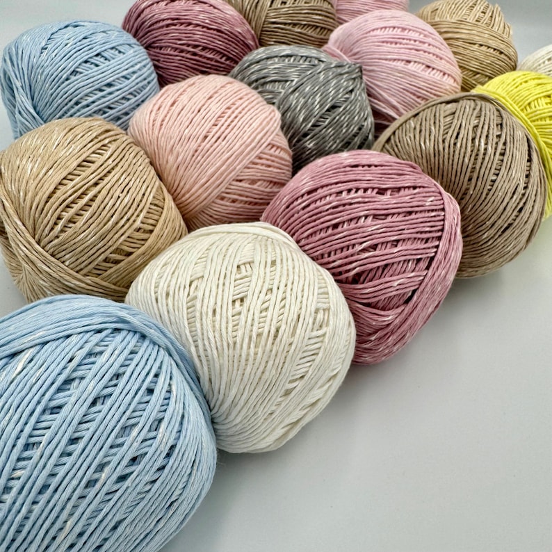 May include: A collection of yarn balls in various colors, including pink, beige, blue, and white. The yarn is made of natural fibers and has a textured appearance.