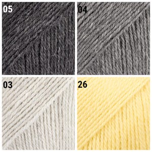 K&ouml;nnte beinhalten: Nahaufnahme von vier Garnkn&auml;ueln in verschiedenen Farben. Oben links dunkelgrau mit der Nummer "05". Oben rechts grau mit der Nummer "04". Unten links cremewei&szlig; mit der Nummer "03". Unten rechts gelb mit der Nummer "26".