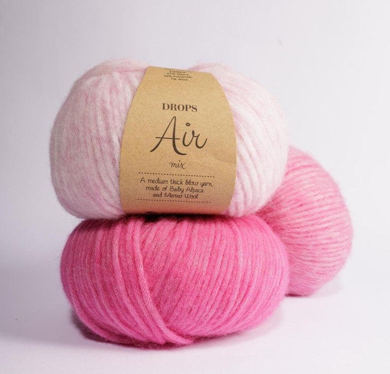 May include: Two skeins of yarn, one pink and one ombre pink and white, with a brown label that reads "DROPS Air mix A medium thick blow yarn made of Baby Alpaca and Merino Wool"