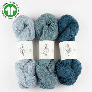 May include: Three skeins of yarn in shades of blue, teal, and light blue. The yarn is labeled "Loch Lomond Lace" and is made of 100% organic wool. The yarn is certified by the Global Organic Textile Standard (GOTS).