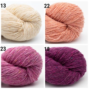 May include: Four skeins of yarn in different colors: cream, peach, pink, and purple. Each skein is made of a soft, textured yarn with flecks of color throughout.