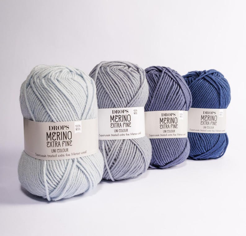 K&ouml;nnte beinhalten: Vier Kn&auml;uel Garn in Blaut&ouml;nen, von hell bis dunkel. Jedes Kn&auml;uel ist mit "DROPS MERINO EXTRA FINE UNI COLOUR" beschriftet und tr&auml;gt den Text "Superwash treated extra fine Merino wool".