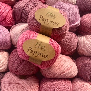May include: A pile of pink yarn balls with brown labels that read "fibra natura Papyrus".