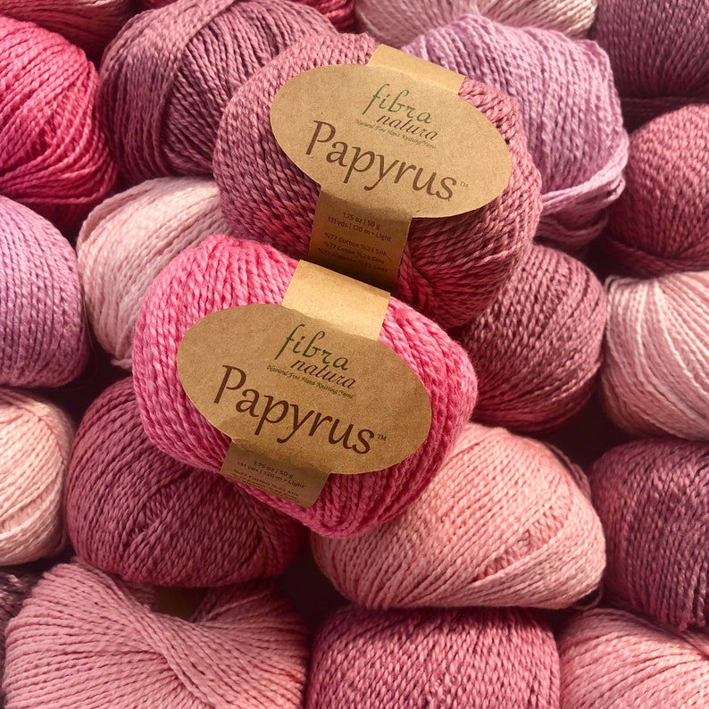 May include: A pile of pink yarn balls with brown labels that read "fibra natura Papyrus".