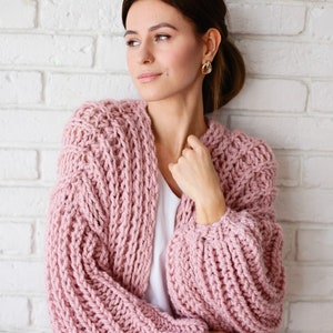 Pu&ograve; includere: Un cardigan rosa lavorato a maglia con una vestibilit&agrave; ampia e maniche lunghe. Il cardigan &egrave; realizzato con un filato spesso e ha uno stile rilassato e casual.