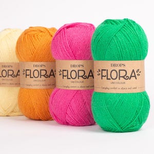 K&ouml;nnte beinhalten: Vier Kn&auml;uel Drops Flora Uni Colour Garn in Gelb, Orange, Pink und Gr&uuml;n. Jedes Kn&auml;uel hat ein braunes Papieretikett mit Markennamen und Produktdetails. Das Garn besteht aus Alpaka und Wolle. Ideal zum Stricken und H&auml;keln.