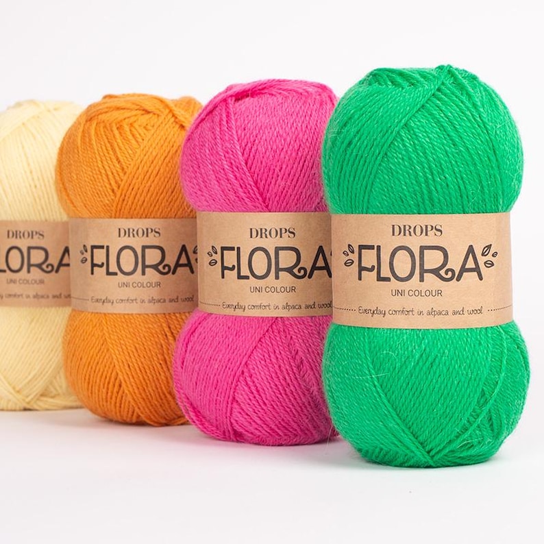 K&ouml;nnte beinhalten: Vier Kn&auml;uel Drops Flora Uni Colour Garn in Gelb, Orange, Pink und Gr&uuml;n. Jedes Kn&auml;uel hat ein braunes Papieretikett mit Markennamen und Produktdetails. Das Garn besteht aus Alpaka und Wolle. Ideal zum Stricken und H&auml;keln.