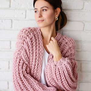 Pu&ograve; includere: Un cardigan rosa lavorato a maglia con una vestibilit&agrave; ampia e maniche lunghe. Il cardigan &egrave; realizzato con un filato spesso e ha uno stile rilassato e casual.