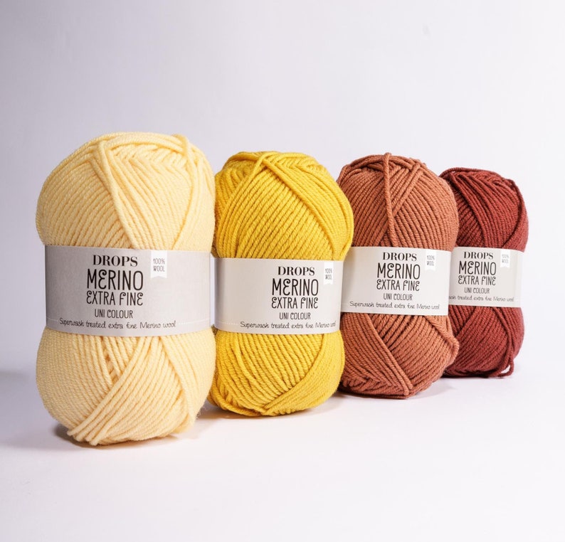 K&ouml;nnte beinhalten: Vier Kn&auml;uel Drops Merino Extra Fine Garn in Gelb, Orange und Braun. Das Garn ist superwash behandelt und besteht aus 100% Wolle.