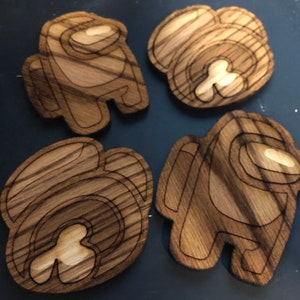 Pode incluir: Quatro recortes de madeira do popular personagem do jogo Among Us. Os recortes são marrons com um padrão de grão de madeira e têm um contorno marrom claro.