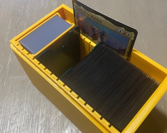 Könnte beinhalten: Eine gelbe Plastik-Kartenbox mit einem Kartenspiel im Inneren. Die oberste Karte ist sichtbar und trägt die Aufschrift "Gavl, Nest Warden".