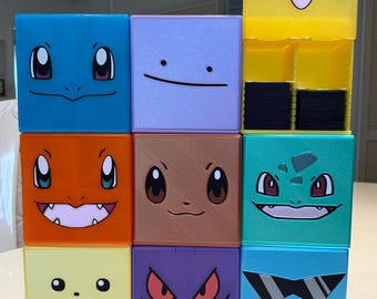 Può includere: Nove scatole colorate a forma di cubo con diversi personaggi Pokémon su ogni lato. Le scatole sono impilate in tre file di tre. La scatola superiore presenta un Pikachu giallo con le guance rosse. Le scatole sono in plastica e hanno una finitura lucida.