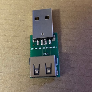 May include: A green circuit board with a USB connector on one end and a USB-A connector on the other end. The board has the text "2744623E-Y53-220304" and "CN1" printed on it.